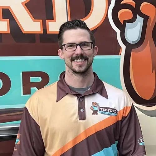 A Tedford technician with glasses smiling in front of a Tedford van